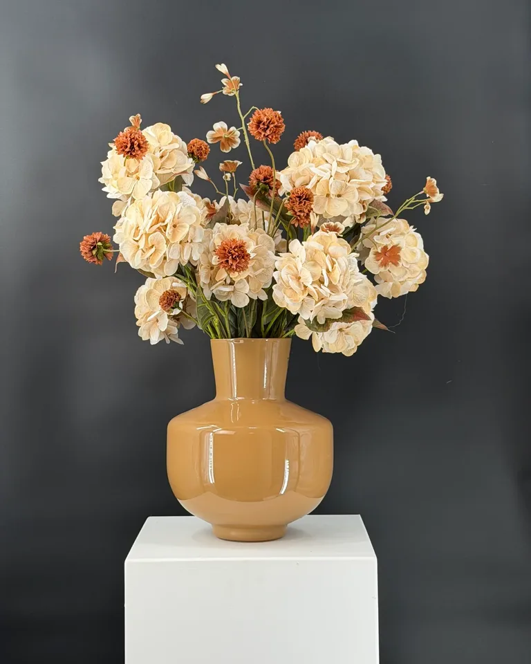 Celeste: rond boeket met crème hortensia, bruin-crème begonia en bruine korenbloem in een okerkleurige vaas.