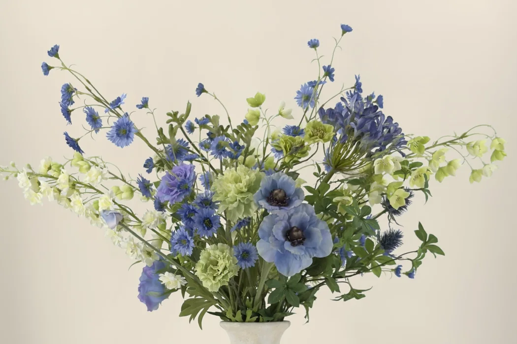Blauw en limegroen kunstboeket met hoge takken en lagere bloemen tegen een warme beige achtergrond.