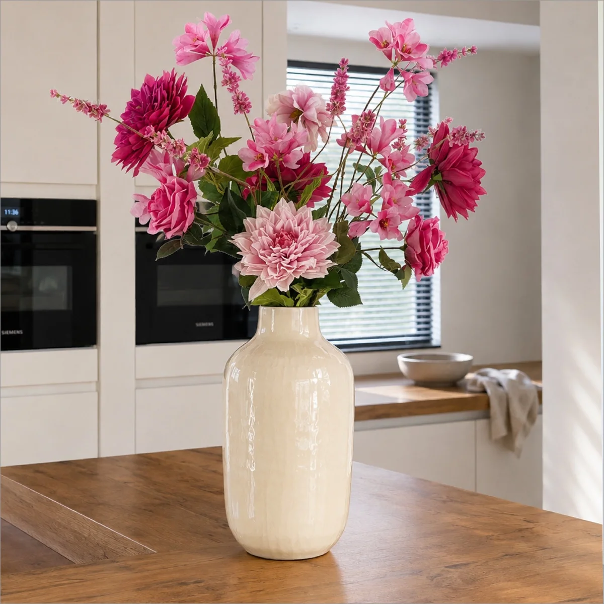 Roze kunstbloemen in een crèmekleurige vaas op een houten kookeiland.