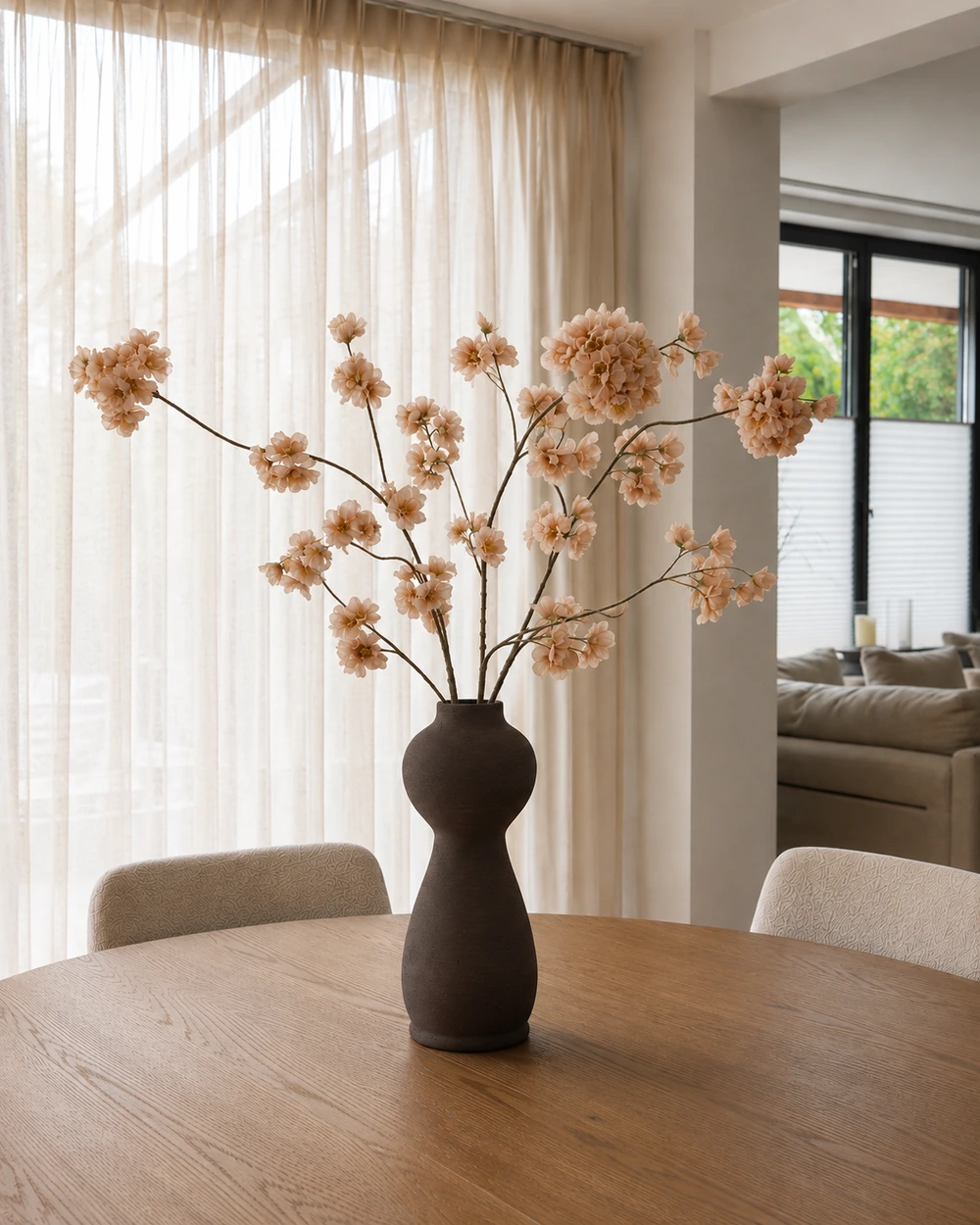Ramo artificial con flores color capuchino en un jarrón oscuro sobre una mesa de comedor redonda