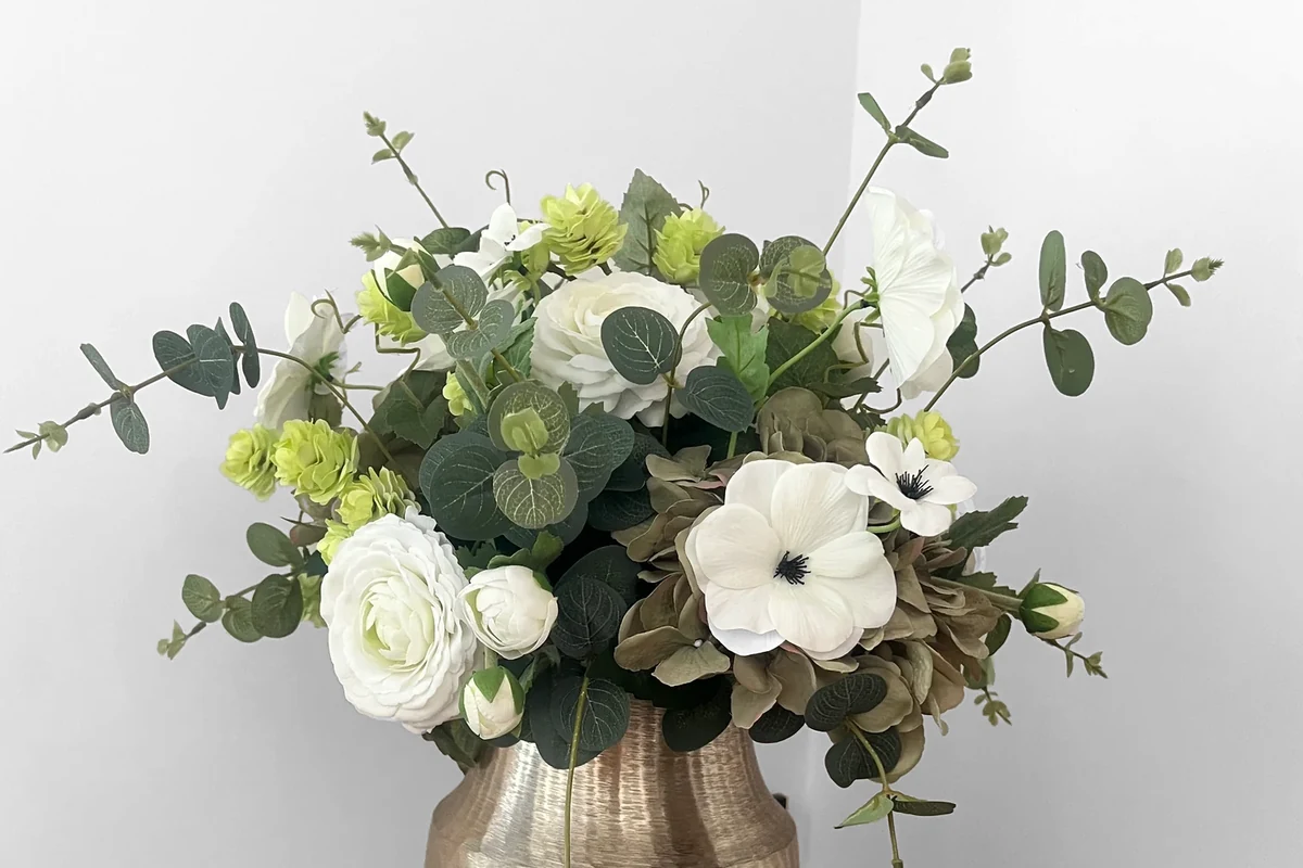 Jetta, een kunstboeket met witte en limegroene bloemen, taupekleurige hortensia en groen blad in een goudkleurige vaas.
