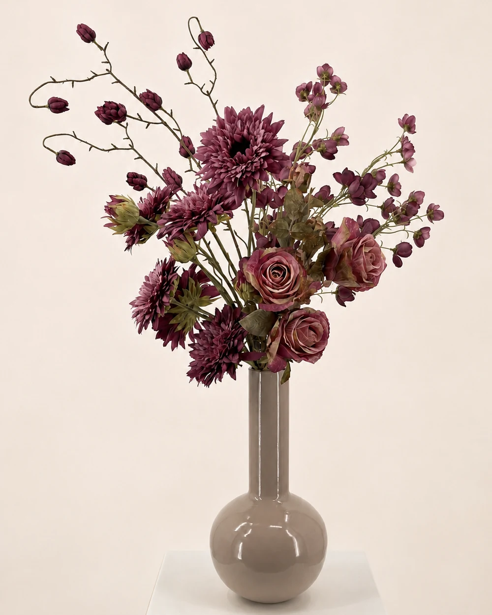 Violetta met paarse en bordeauxkleurige kunstbloemen in een taupekleurige vaas met een lange smalle hals.