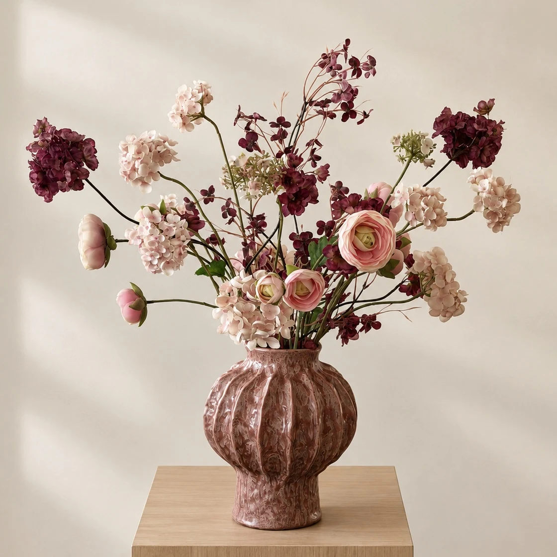 Mikela met roze en bordeauxrode kunstbloemen in een roze vaas op een licht eiken zuil.